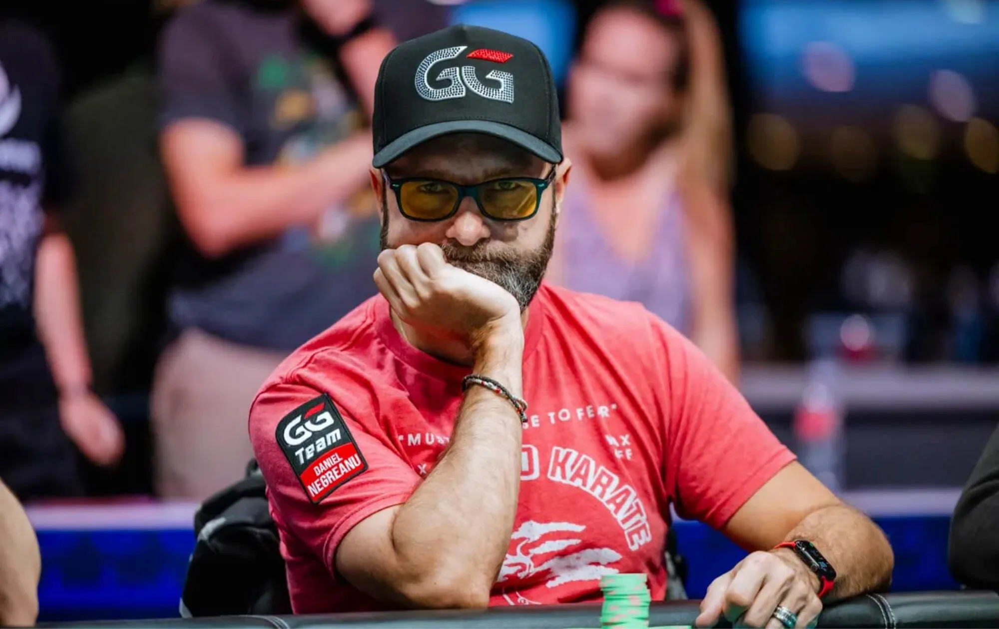 Daniel Negreanu com amão na Boca sentado em uma mesa de poker segurando fichas com amão esquerda e a mão direta está na boca - www.rakebackpokerworld.com